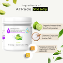 A white tub of ATPade Steady Steady Active hydration powder in the Lime flavor, shown on a light cream background with floating lime slices and text callouts detailing its ingredients.